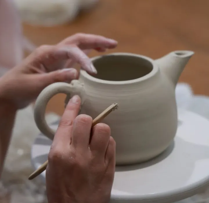 Mains façonnant une théière en argile pendant un cours à l’atelier